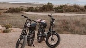 Dues bicicletes aparcades sobre sorra, amb una platja i l'oceà al fons.