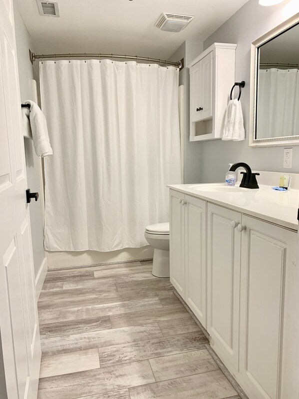 A bathroom with a shower curtain, toilet, and white cabinets.