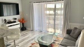 Una sala de estar moderna con una mesa de centro de vidrio, un sofá gris y una zona de comedor con sillas blancas.