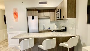Una cocina moderna con una isla central, taburetes blancos, electrodomésticos de acero inoxidable y armarios de madera.