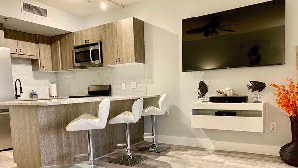 Una cocina moderna con una isla central, taburetes de bar, microondas y un televisor de pantalla plana montado en la pared.