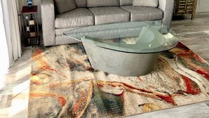 Una sala de estar moderna con un sofá gris, una mesa de centro de vidrio y una alfombra abstracta y colorida.