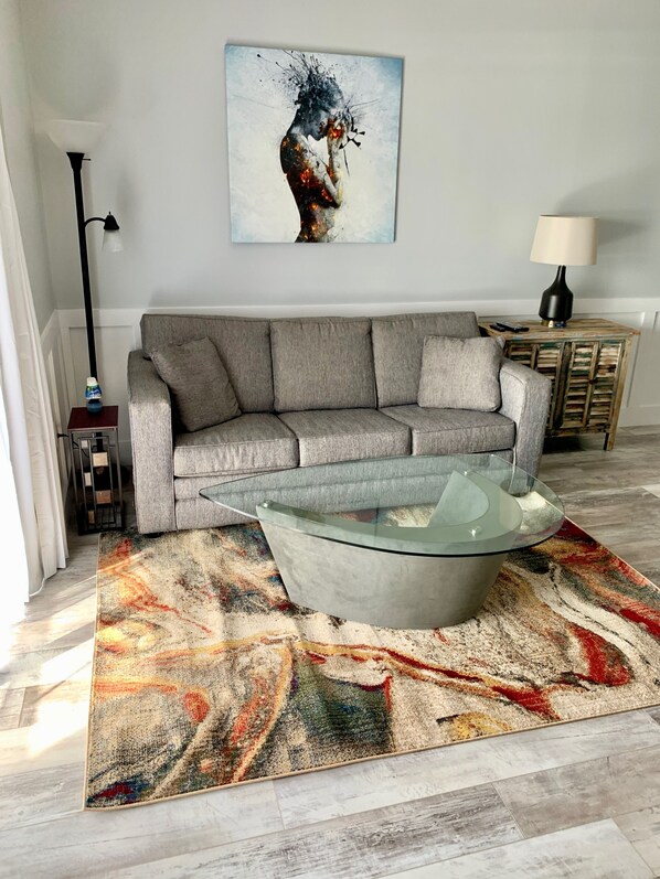 Una sala de estar moderna con un sofá gris, una mesa de centro de vidrio y una alfombra abstracta y colorida.