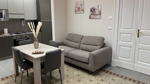 A compact living space with a kitchenette, a grey sofa, a dining table with chairs, and a door. - Families, groups of friends, looking for a comfortable apartment in the Acese Baroque (Acireale)