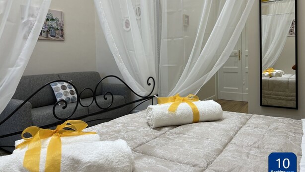 A hotel room with a bed, a grey sofa, a mirror, and a window with sheer curtains. - Families, groups of friends, looking for a comfortable apartment in the Acese Baroque (Acireale)