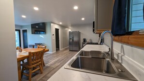 Een moderne keuken met een roestvrijstalen spoelbak, een koelkast en een eethoek met houten stoelen.