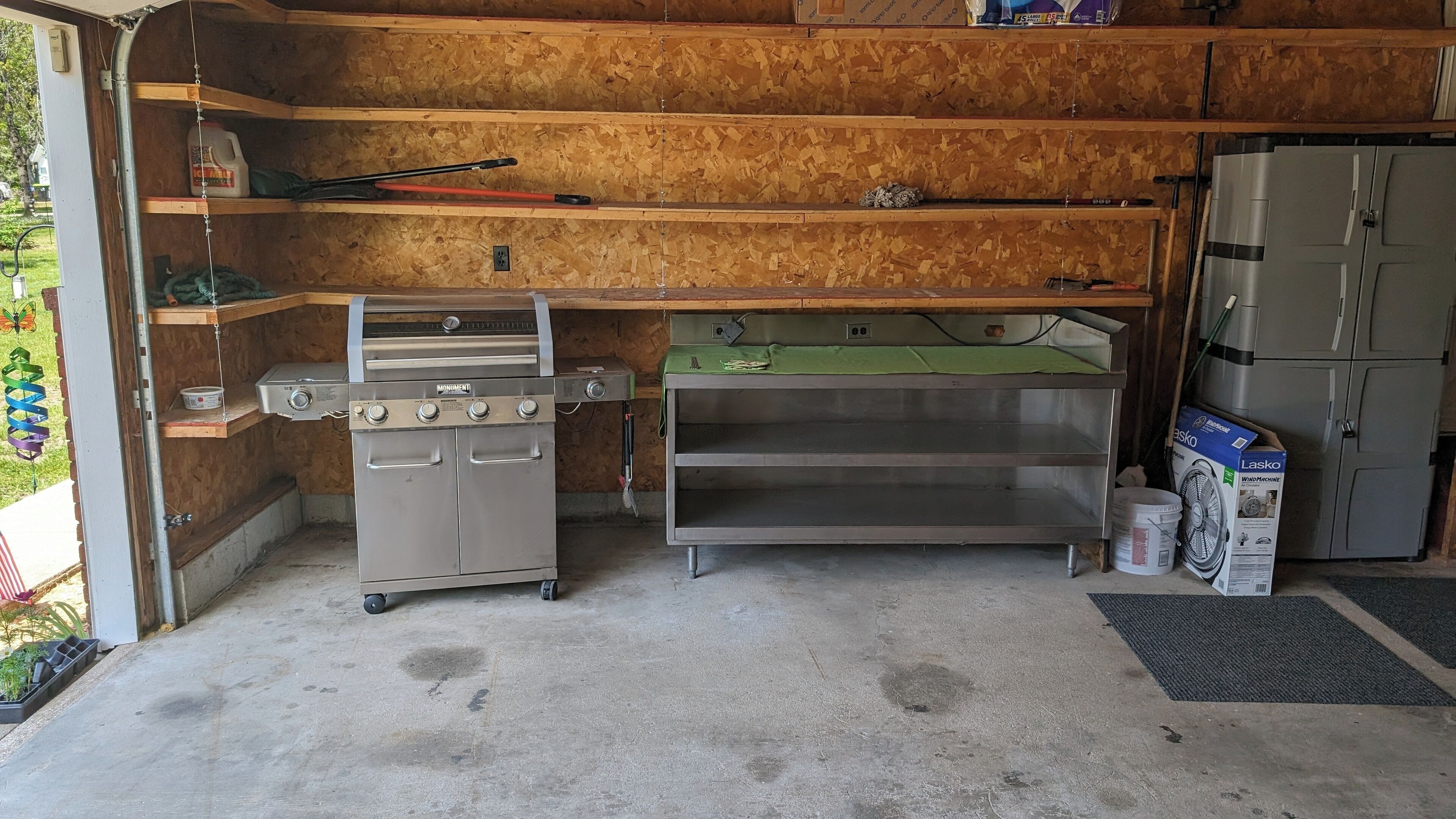 Un garaje con una parrilla de acero inoxidable, un refrigerador y un banco de trabajo.