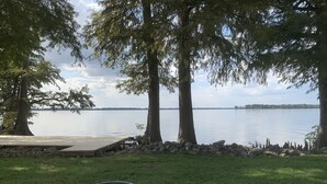 Terraza junto al lago con una parrilla de metal, rodeada de árboles y un muro de piedra.