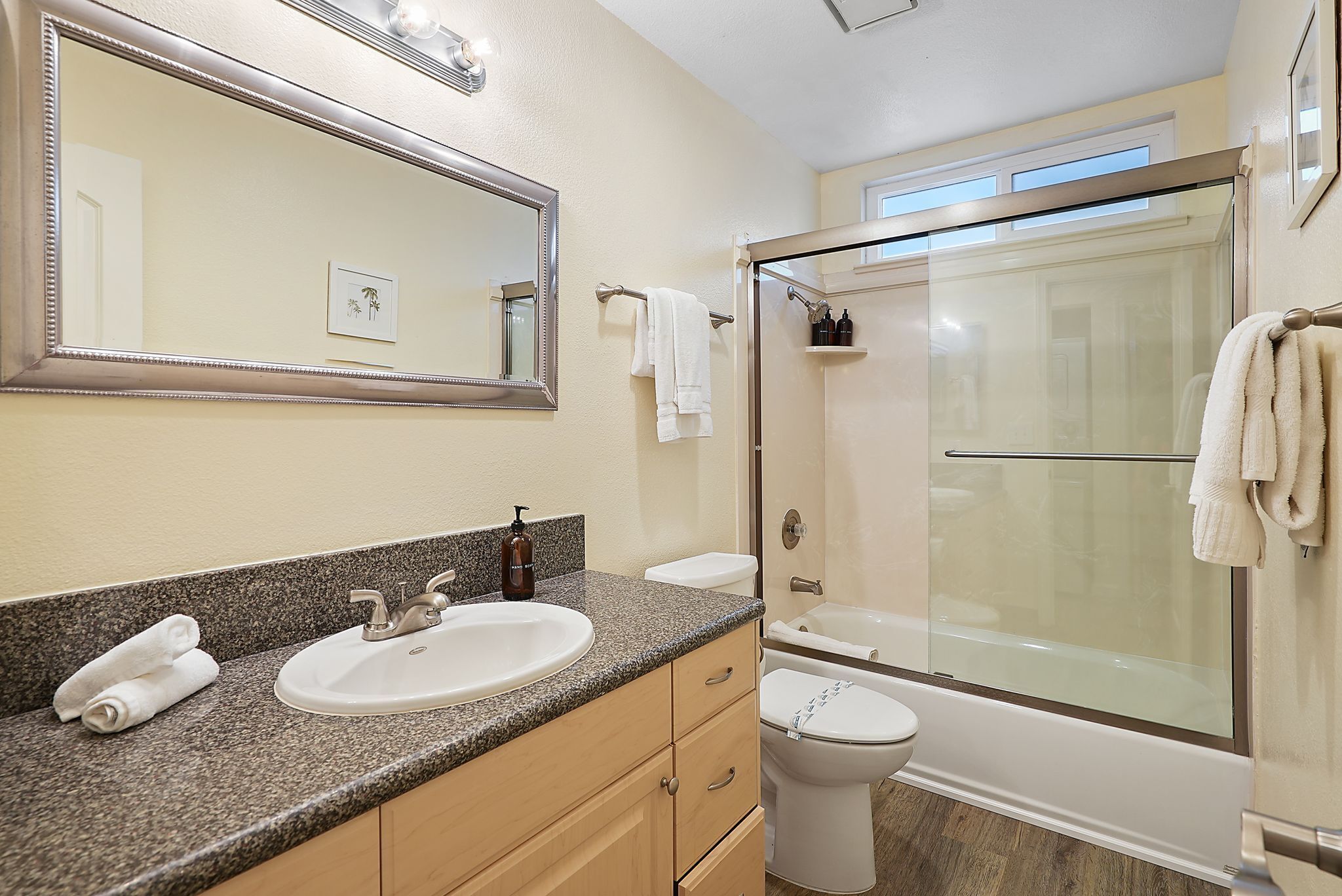 A bathroom with a granite countertop, a sink, a toilet, a glass-enclosed shower, and a large mirror.