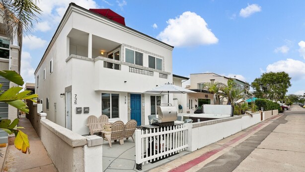A two-story white house with a balcony, a barbecue grill, and a red umbrella. - Ocean View Perfection - Parking, W/D, Pet Friendly & Steps to Sand (Mission Beach)