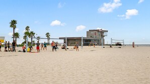 A beach volleyball court with players and spectators, palm trees, and a lifeguard tower in the background. - Ocean View Perfection - Parking, W/D, Pet Friendly & Steps to Sand (Mission Beach)