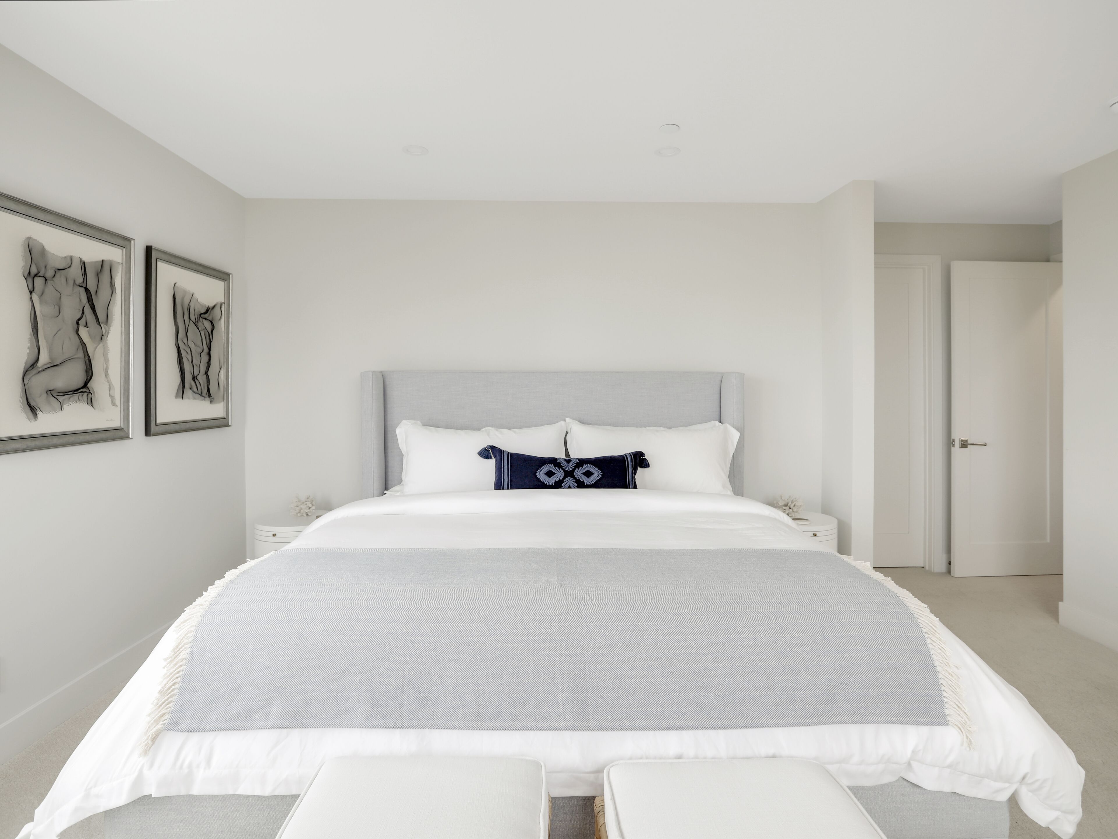 A modern bedroom with a large bed, a bedside table, and two framed artworks on the wall.