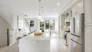 A modern kitchen with white cabinetry, stainless steel appliances, and a central island. - Designer Luxury Coastal Home with Panoramic Ocean Views, Rooftop Deck, & Fire Pit (La Jolla)
