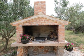 A brick-built outdoor oven with a chimney, surrounded by olive trees.