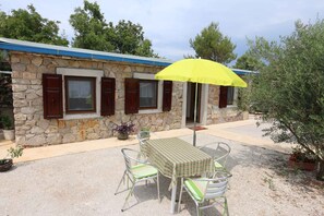 A stone building with a blue roof, a table with chairs, and a yellow umbrella. - Holiday home in a private olive grove (Šilo)