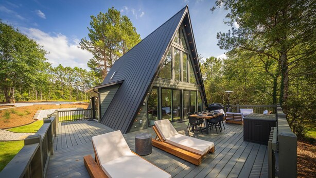 Ein modernes Haus mit Satteldach, einer Terrasse mit Liegestühlen und einem Essbereich.