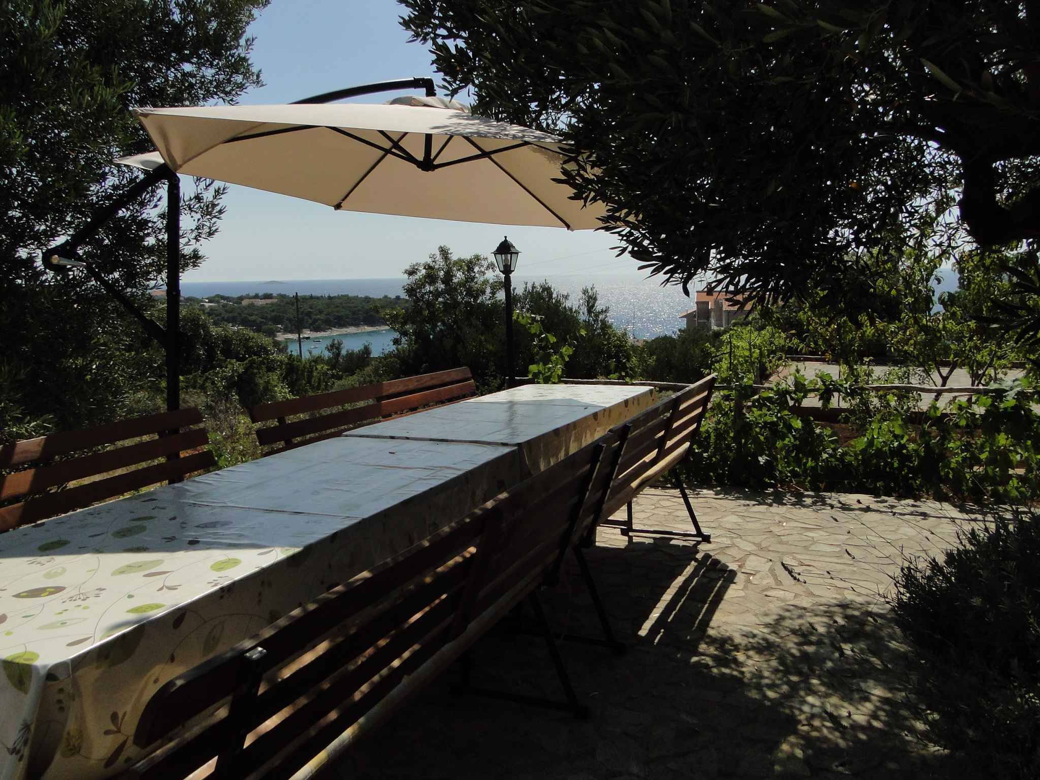 An outdoor dining area with a table and benches, a large umbrella, and a view of the sea.