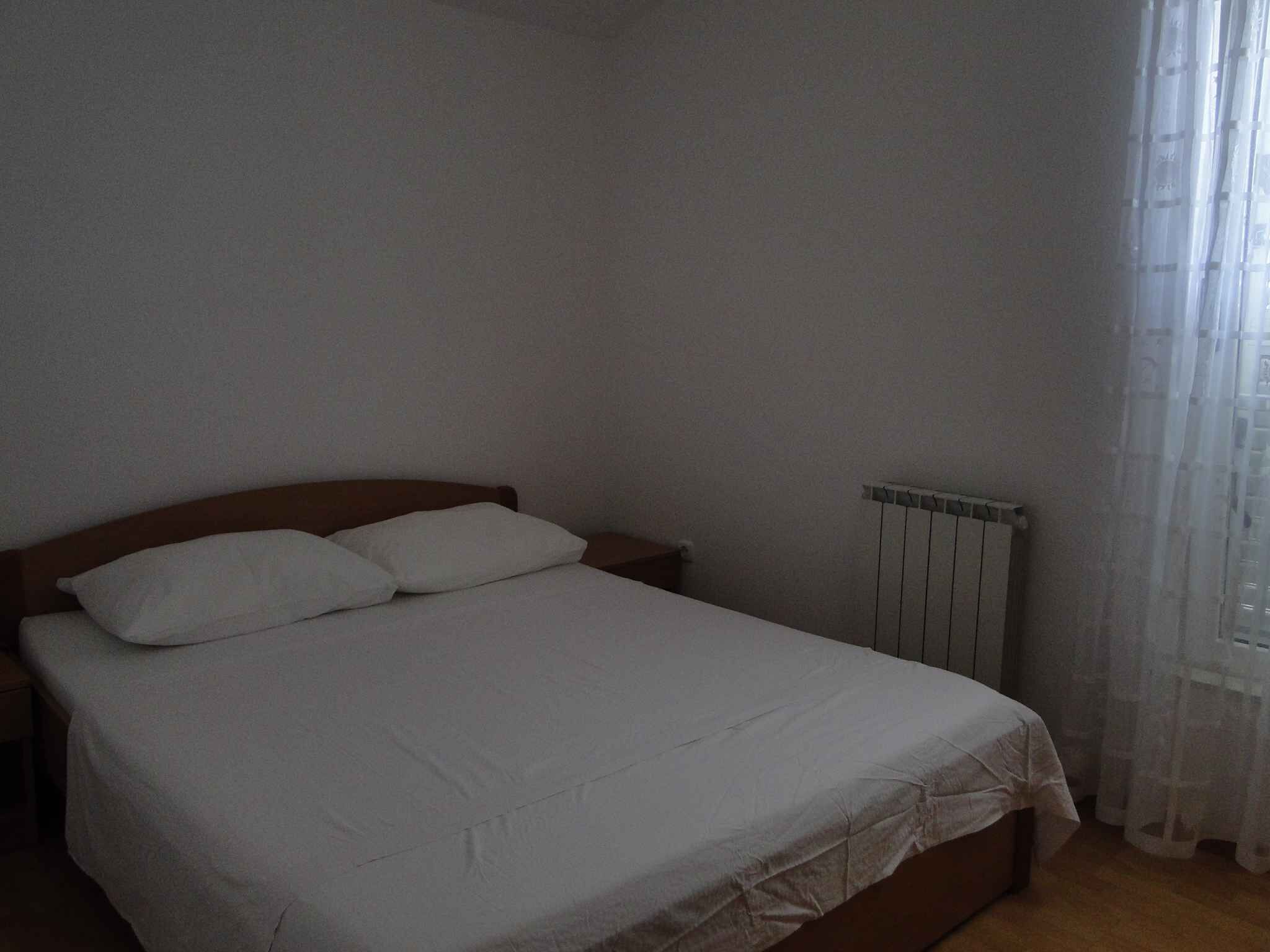 Een slaapkamer met een enkel bed, een houten hoofdbord, een witte dekbedovertrek en een radiator.