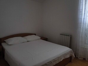 Un dormitorio con una cama individual, cabecera de madera, edredón blanco y un radiador.