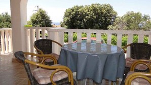 An outdoor patio with a round table and wicker chairs, surrounded by a white fence and greenery.
