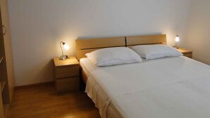 A single bed with a wooden headboard, two bedside tables with lamps, and a plain white wall.