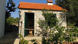 A stone building with a red-tiled roof, a green door, and a small porch area.