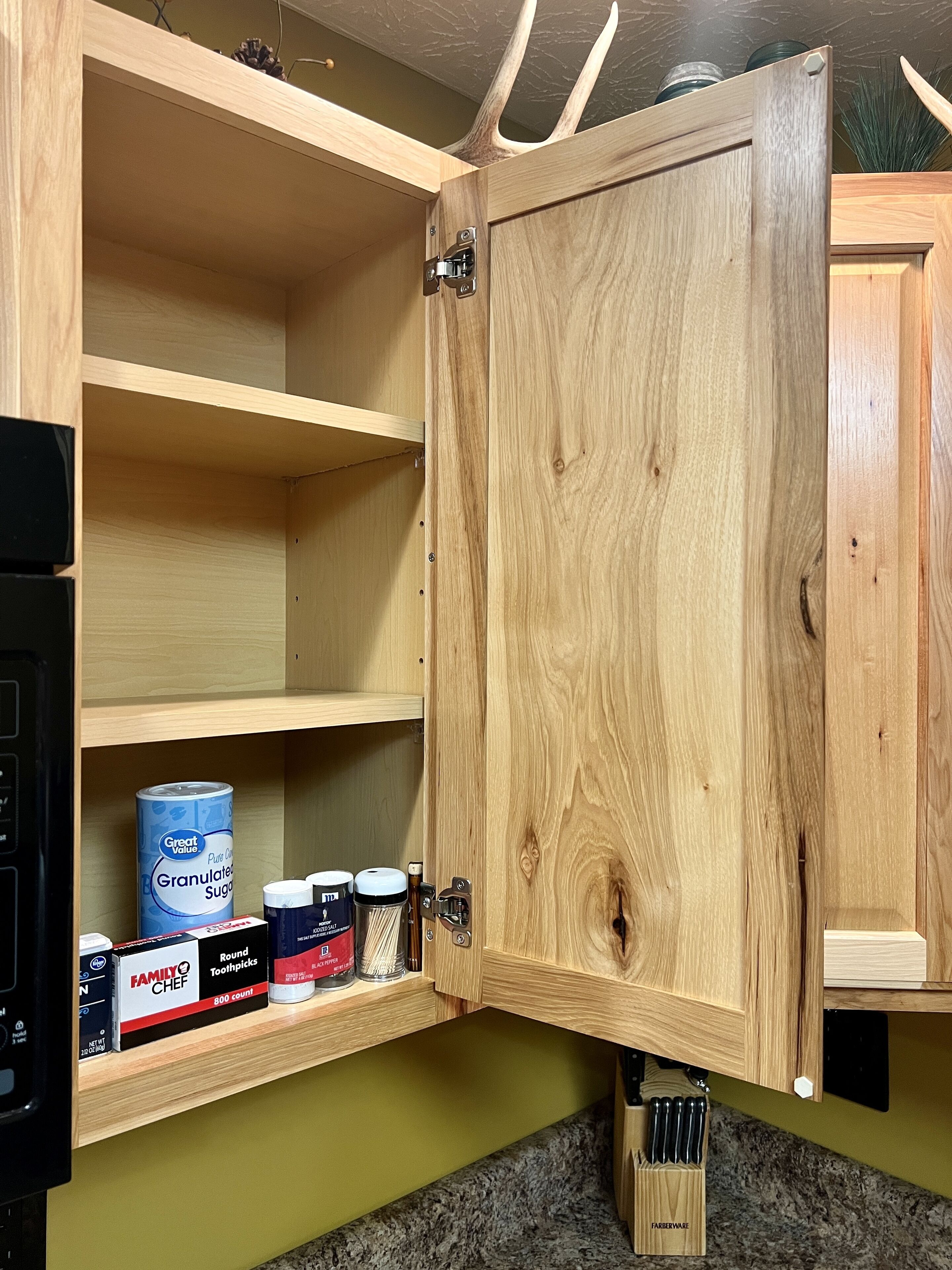 Una cocina con armarios de madera, encimera de granito y una repisa con utensilios de cocina como una lata de azúcar, frascos y una caja de palillos de dientes.