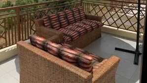 Een balkon met rieten meubilair en een grote parasol.
