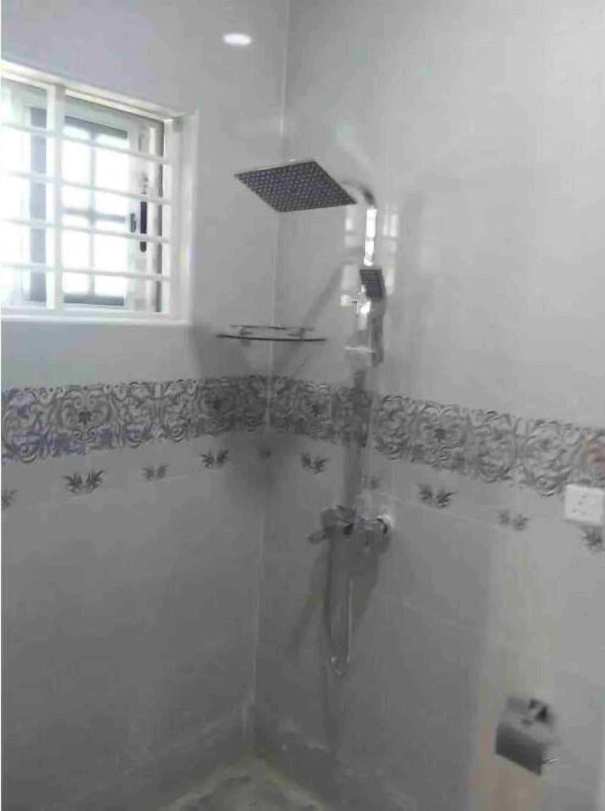 Una ducha con cabezal cuadrado, un estante de cristal y una ventana con barrotes.
