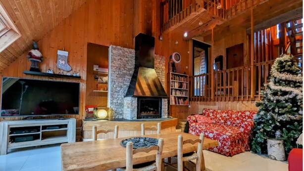 A cozy, rustic interior with a stone fireplace, wooden furniture, and a Christmas tree.