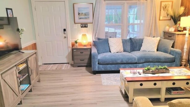A cozy living room with a blue sofa, a wooden coffee table, and a TV on a wooden cabinet. - Beautiful Cottage! 2.5m from I-95,13m to FtBragg (Fayetteville)