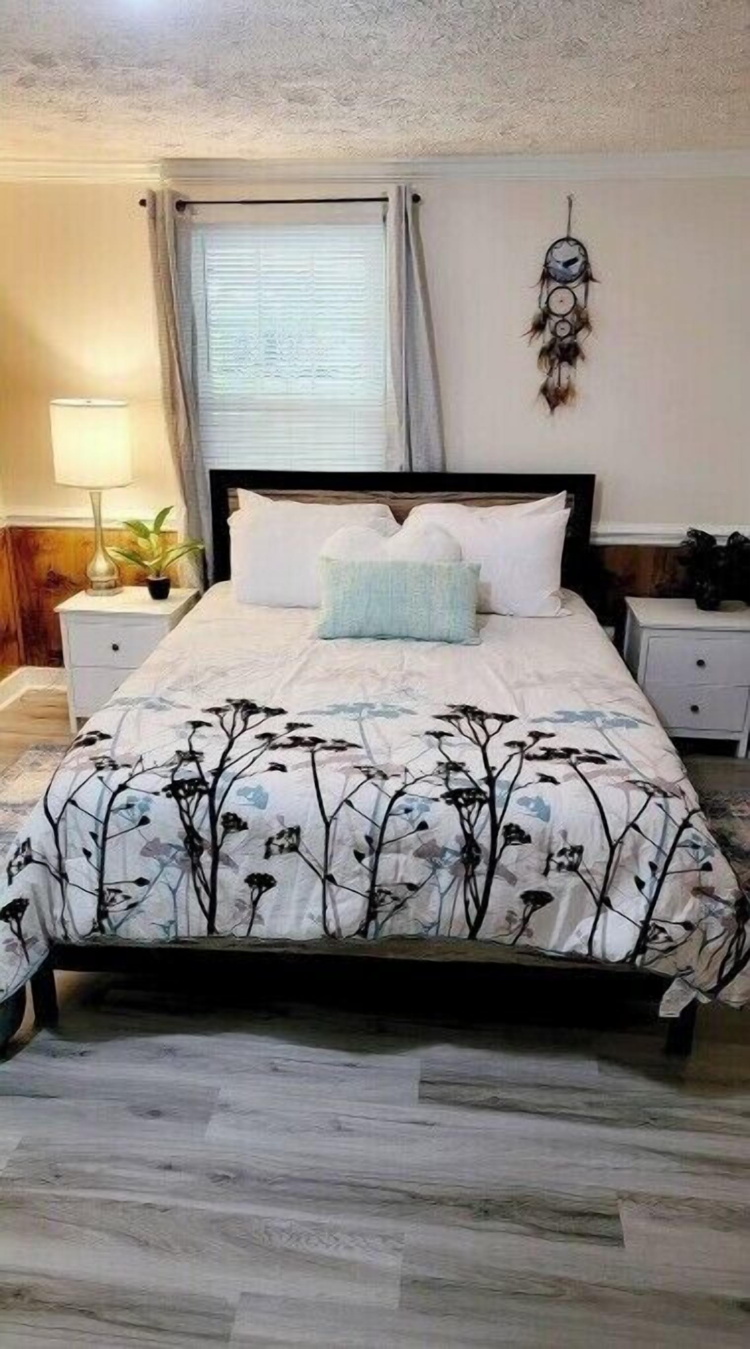 A bedroom with a bed, two bedside tables, a lamp, and a wall decoration.