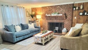 A living room with a blue sofa, a beige sofa, a wooden coffee table, and a brick fireplace. - Beautiful Cottage! 2.5m from I-95,13m to FtBragg (Fayetteville)