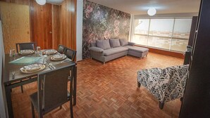 Un salon doté d’un parquet, d’un canapé gris, d’un fauteuil à motifs et d’un coin repas avec une table dressée pour quatre personnes.