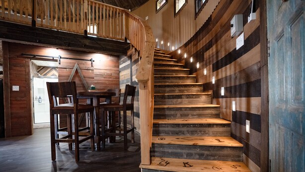 Un escalier en bois, dont les marches sont numérotées, mène à un deuxième étage où se trouvent une salle à manger et des chaises.