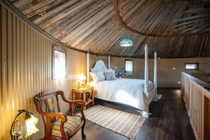 Une chambre à coucher avec un plafond en bois, un lit à baldaquin, une chaise, une table de chevet avec une lampe et une fenêtre.