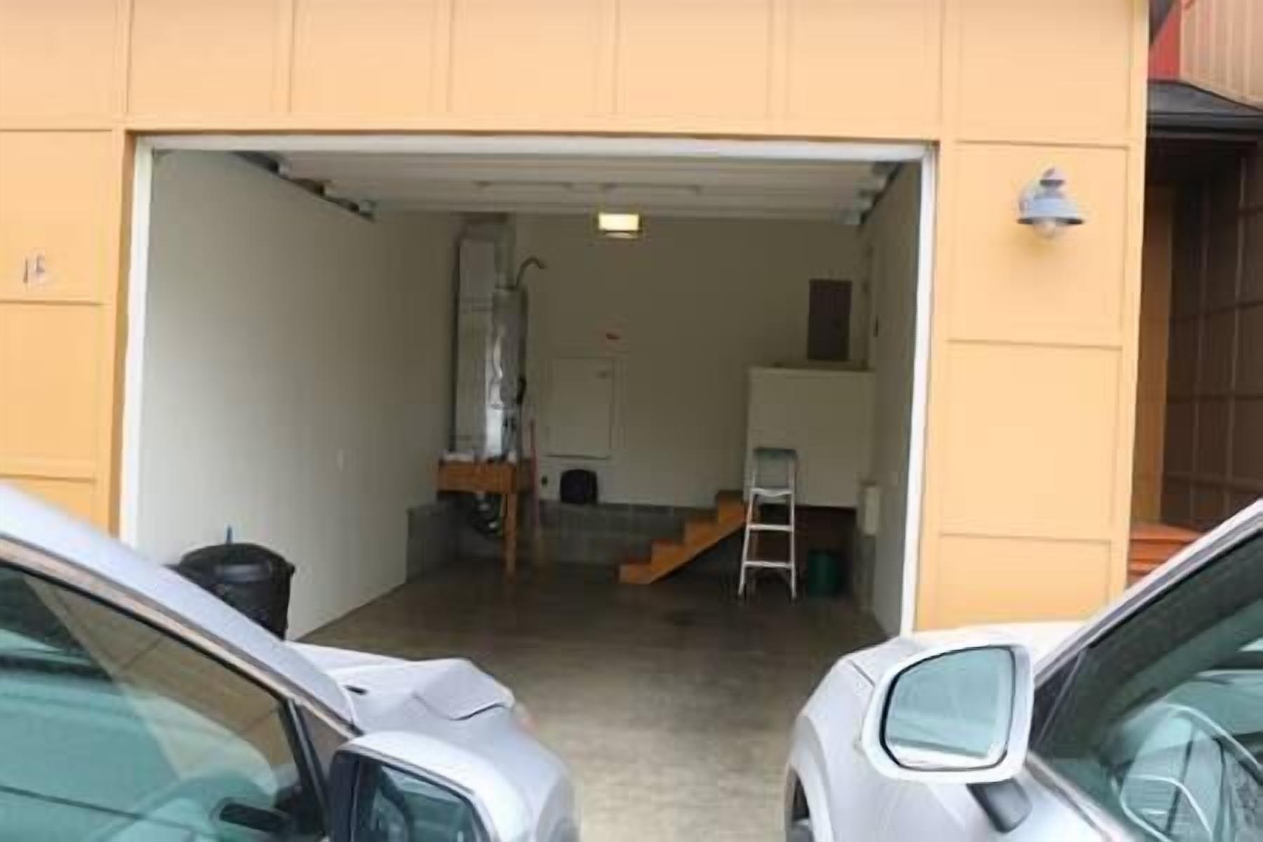A garage with a car parked inside, a ladder, and a staircase leading to an upper level.