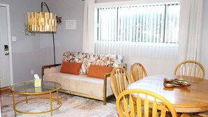 Una sala de estar con sofá, una mesa de centro redonda, una mesa de comedor y sillas.