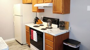 Una cocina compacta con armarios de madera, un refrigerador blanco, una estufa y un cubo de basura.