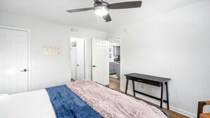 Un dormitorio con cama, ventilador de techo, escritorio y una silla.