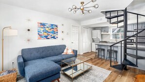 Una sala de estar moderna con un sofá azul, una mesa de centro de vidrio y una lámpara de techo contemporánea.