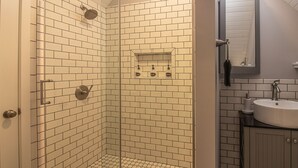 A bathroom with white subway tiles, a shower with a handheld showerhead, a sink with a mirror, and a towel rack. - Quant carriage House, near the city of Asheville and Ashville Airport! (Arden)