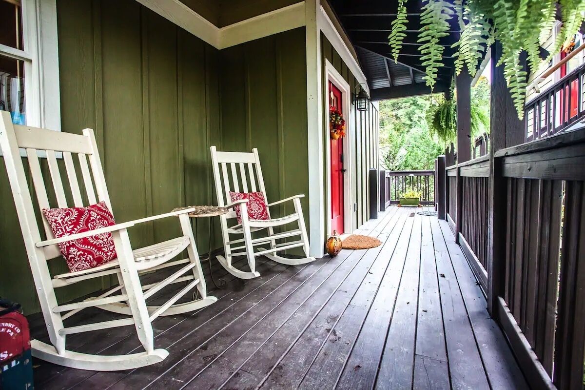 Une véranda avec deux fauteuils à bascule, une porte rouge et une clôture en bois.