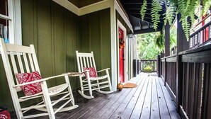 A porch with two rocking chairs, a red door, and a wooden fence.