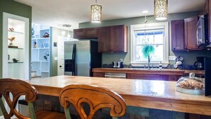 A kitchen with wooden cabinets, a central island with chairs, pendant lighting, and a view of the outdoors.