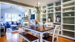 A dining area with a wooden table and white chairs, surrounded by white shelving units with decorative items.
