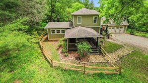 A two-story house with a covered porch and a garage, surrounded by dense forest.