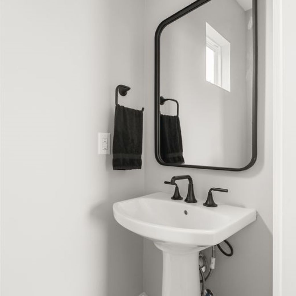 A white bathroom with a pedestal sink, black faucet, and a mirror with a black frame.