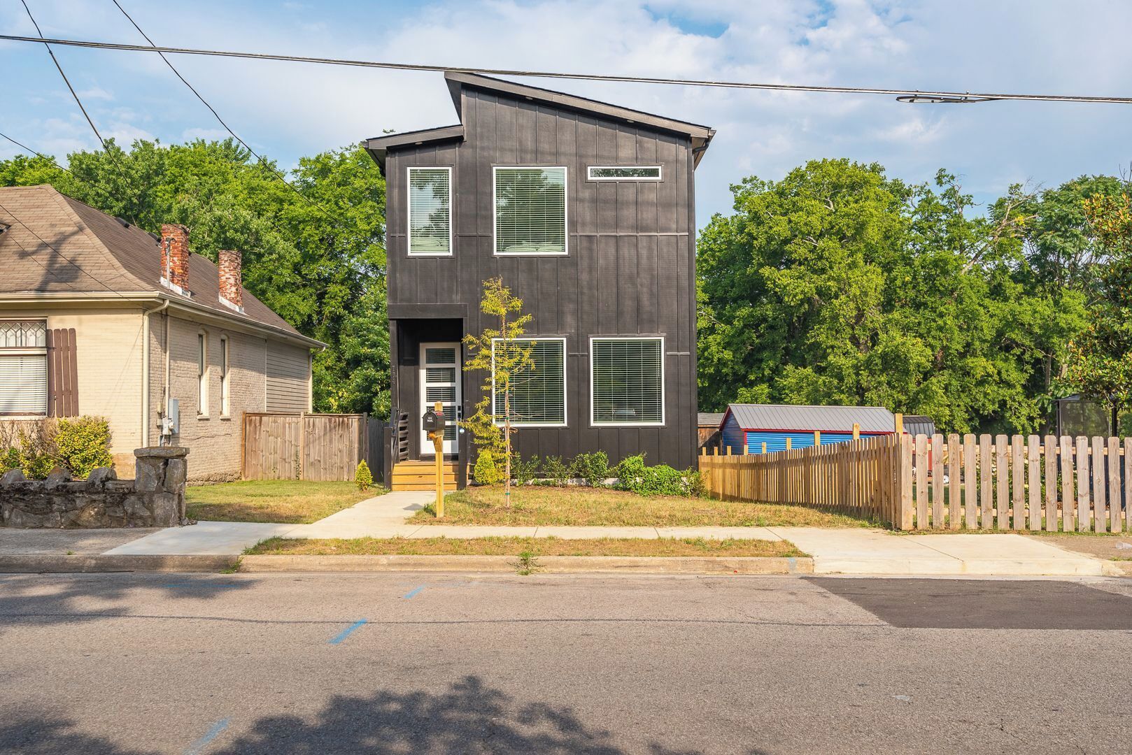 A modern two-story house with a dark exterior, a front porch, and a small tree in the yard.