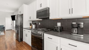 A modern kitchen with white cabinets, a stainless steel refrigerator, a microwave, a gas stove, and a coffee maker. - New home in Nashville built in 2023! Extremely spacious, great for hosting
 (Nashville)